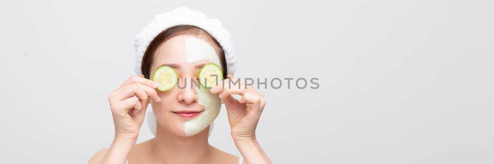 Woman with facial mask holds sliced cucumber, over white banner background by makidotvn