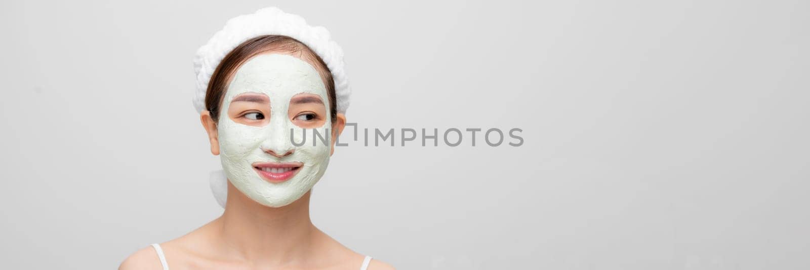 Beautiful young woman with clay facial mask, beauty treatment over white banner by makidotvn