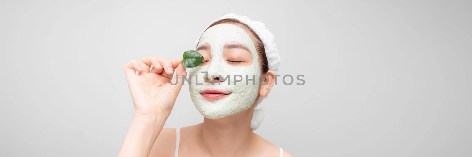 A woman with white nourishing mask on face and green leaf in hand, white banner isolated. by makidotvn