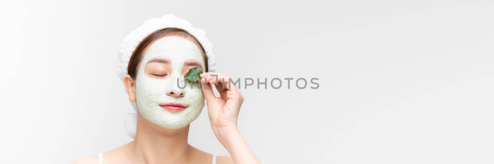 Minimal beauty portrait woman applying white nourishing mask or creme on face, green leaf in hand. banner