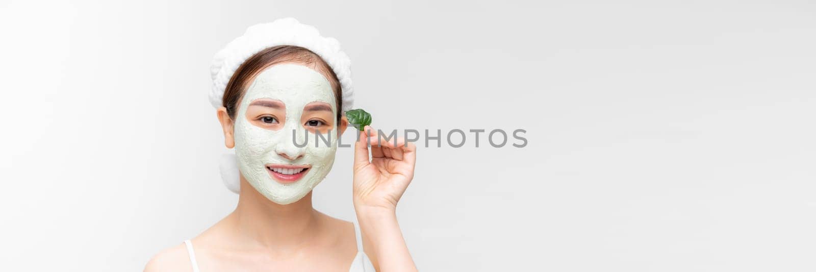 A woman with white nourishing mask on face and green leaf in hand, white banner isolated.