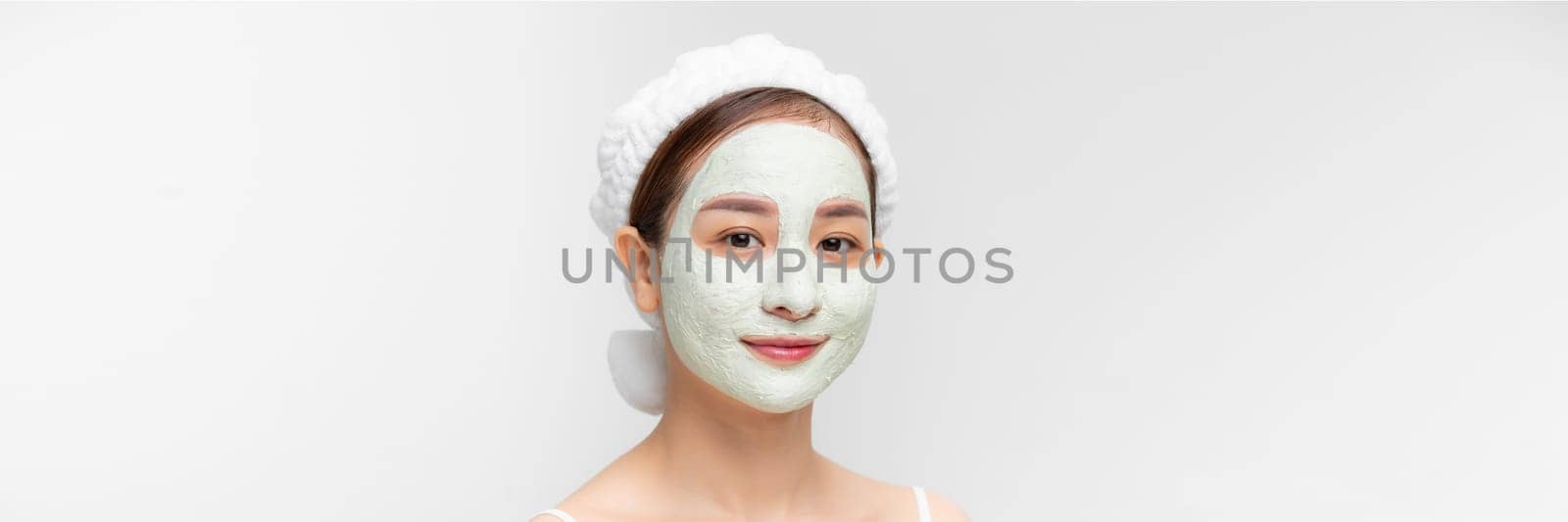 Beautiful young woman with clay facial mask, beauty treatment over white banner by makidotvn