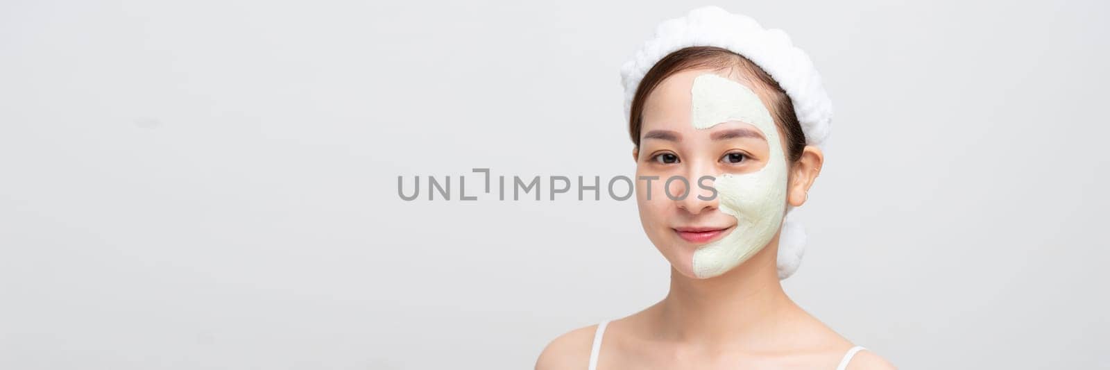 Beautiful woman is getting facial clay mask on white banner background.