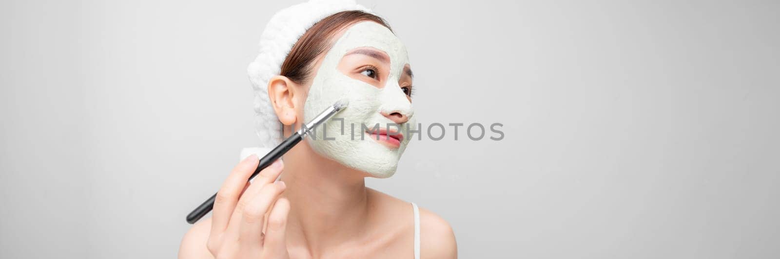 happy woman with a towel on her head apply a cleansing mask on her face by makidotvn