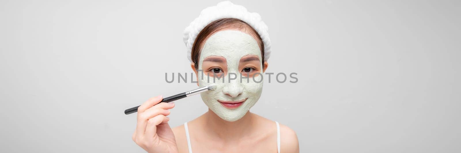 A woman with a green clay cosmetic mask on a white background. Banner wide by makidotvn