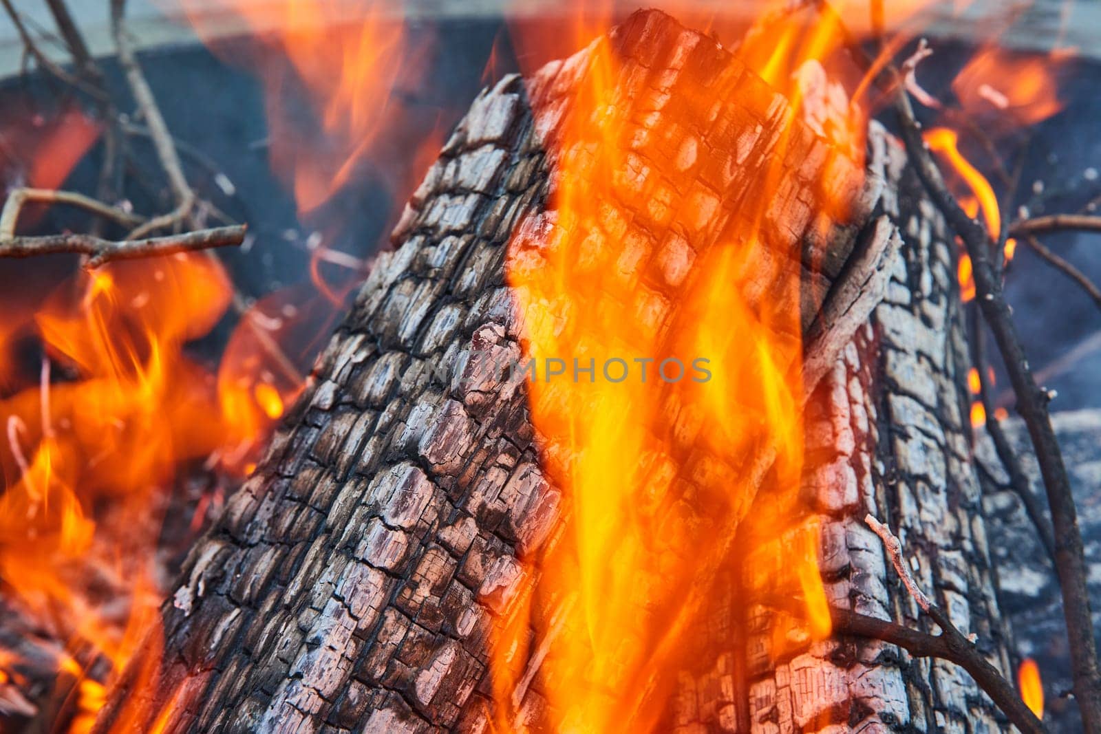 Image of Background asset close up of ashen logs on fire with thick yellow and orange flames in round pit