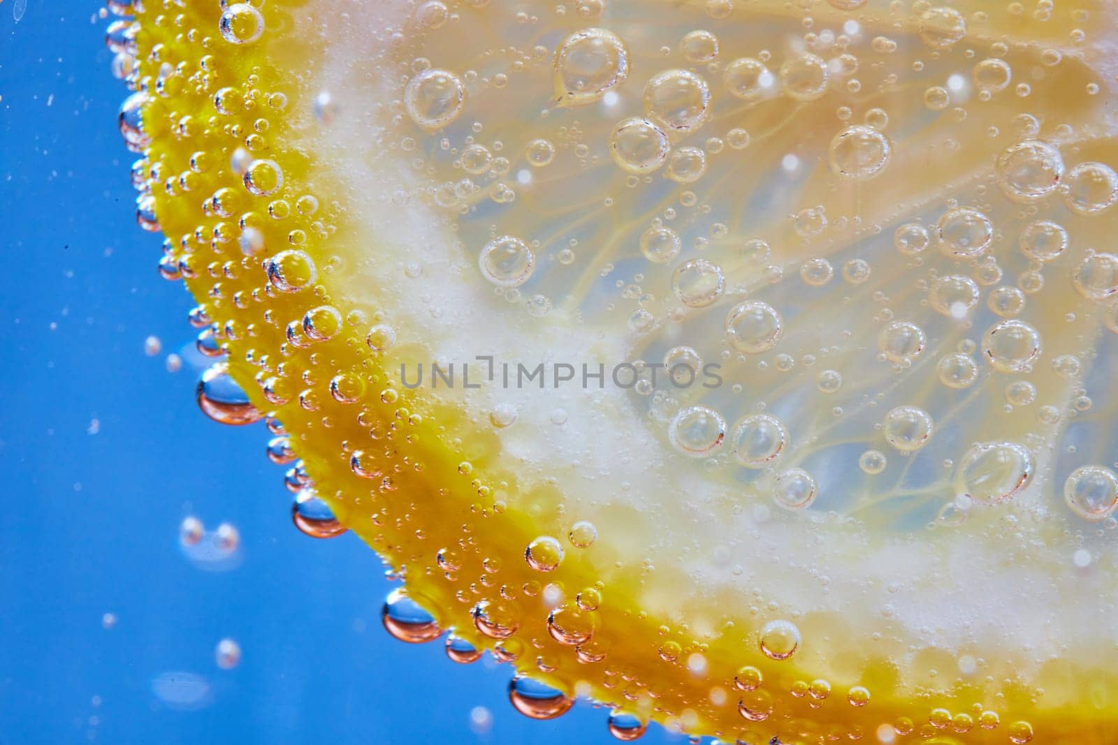 Image of Macro of fizzy bubbles on lemon slice against blue background