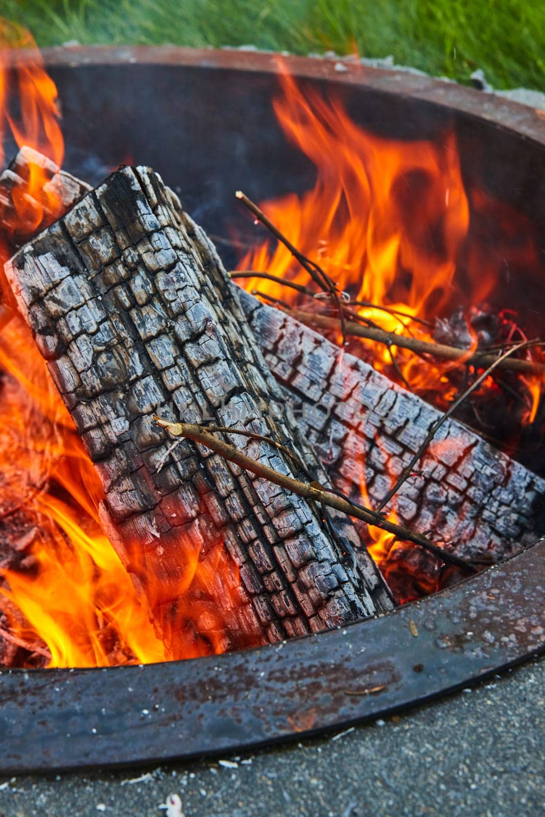 Image of Ashen logs in fire pit with green grass and large orange and yellow flames