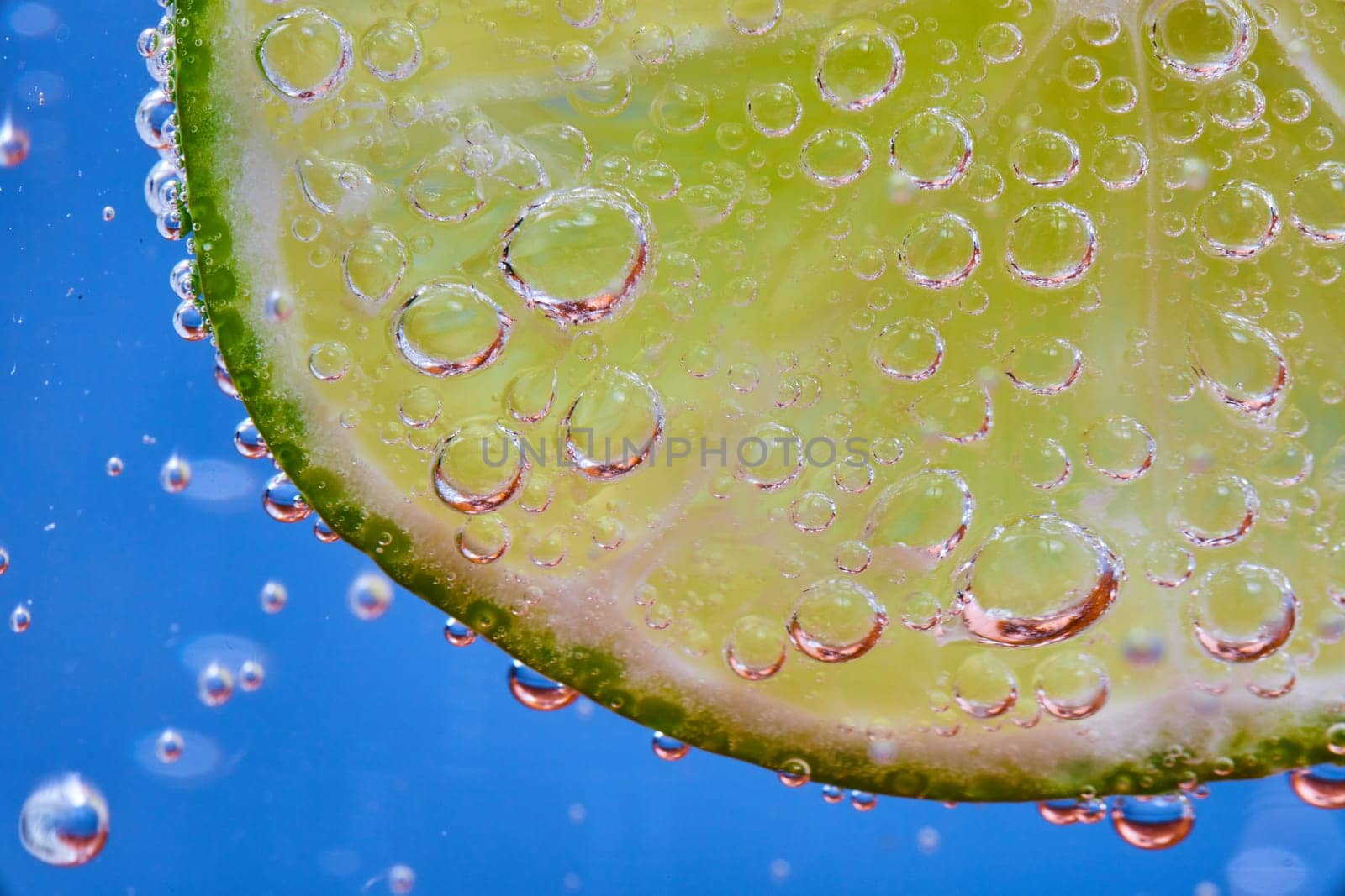 Image of Macro of fizzy bubbles on lime slice against blue background