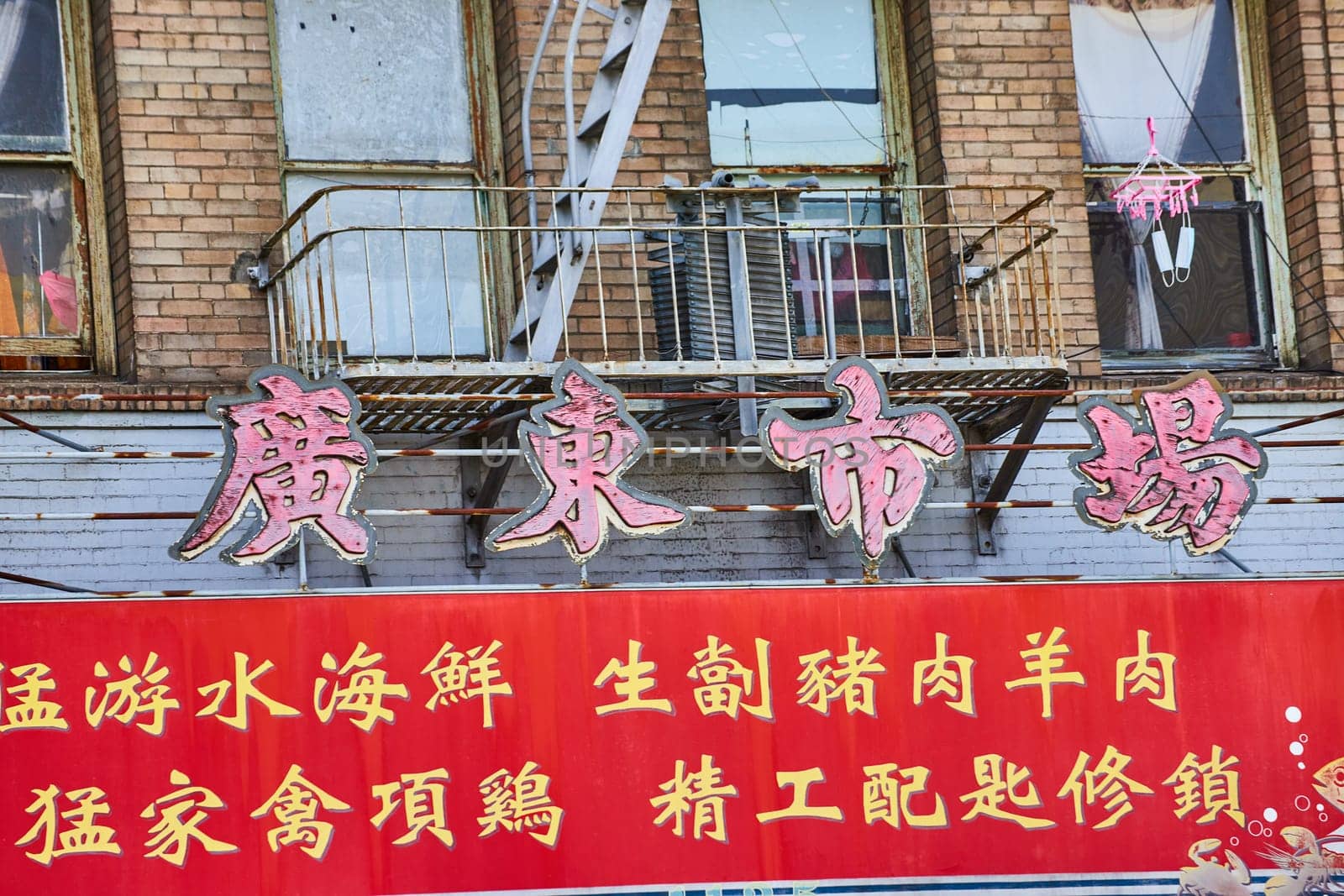Image of Chinese sign below worn down fire escape with red banner in Chinatown