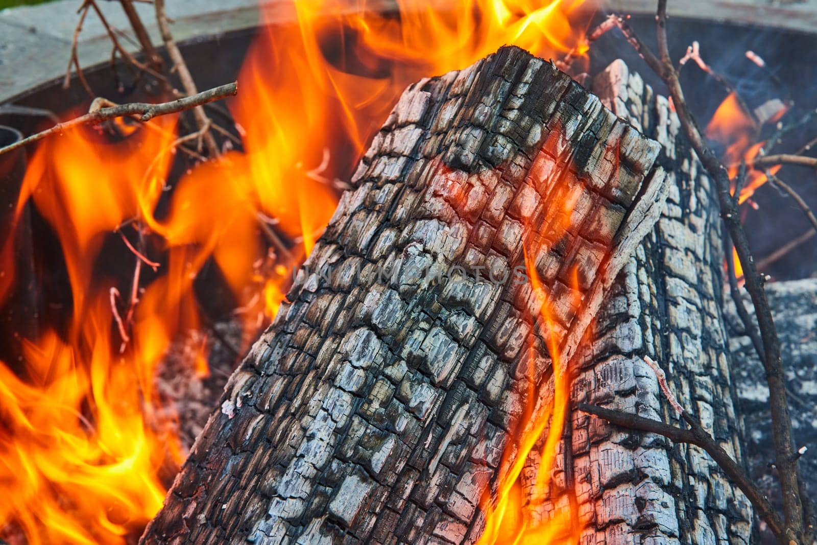 Image of Close up of burning ashen log with orange and yellow flames in round fire pit