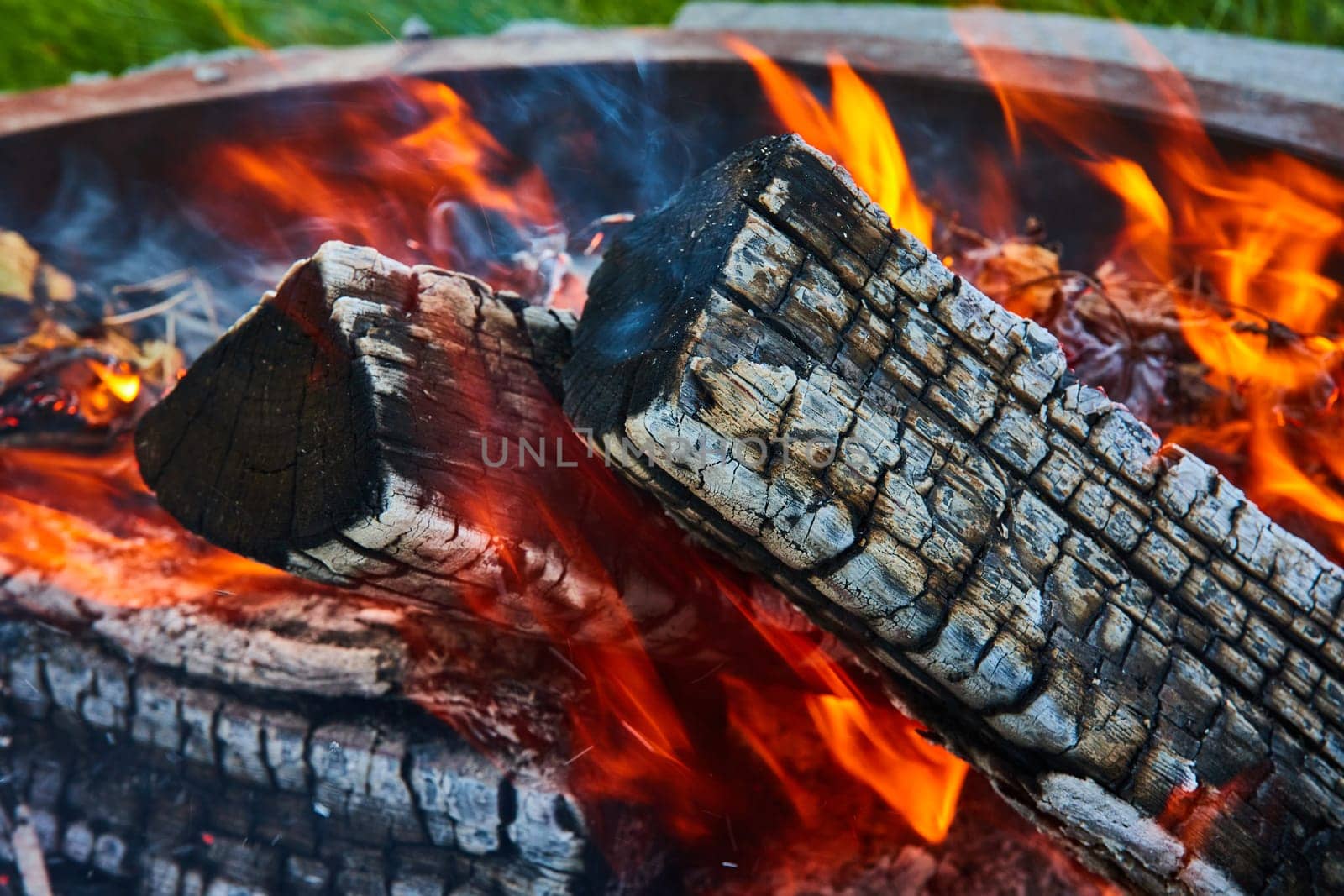 Orange and yellow flames around three logs in firepit close up background asset by njproductions