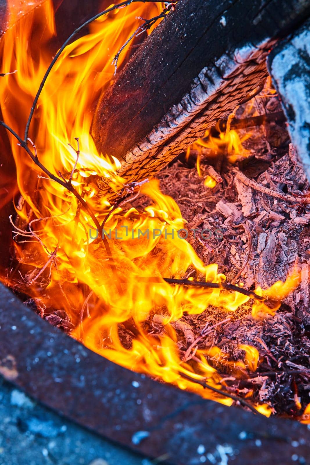 Image of Orange and yellow flames in fire pit with white ashen log and ground