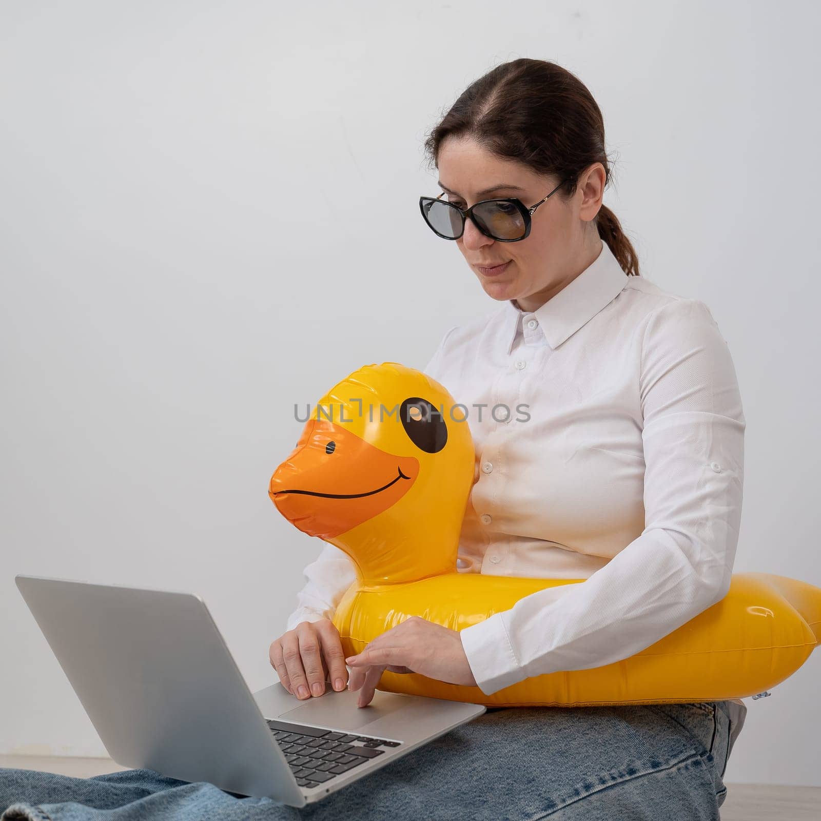 Caucasian woman working at a laptop in sunglasses and in a swimming circle duck. Office worker dreaming of vacation. by mrwed54