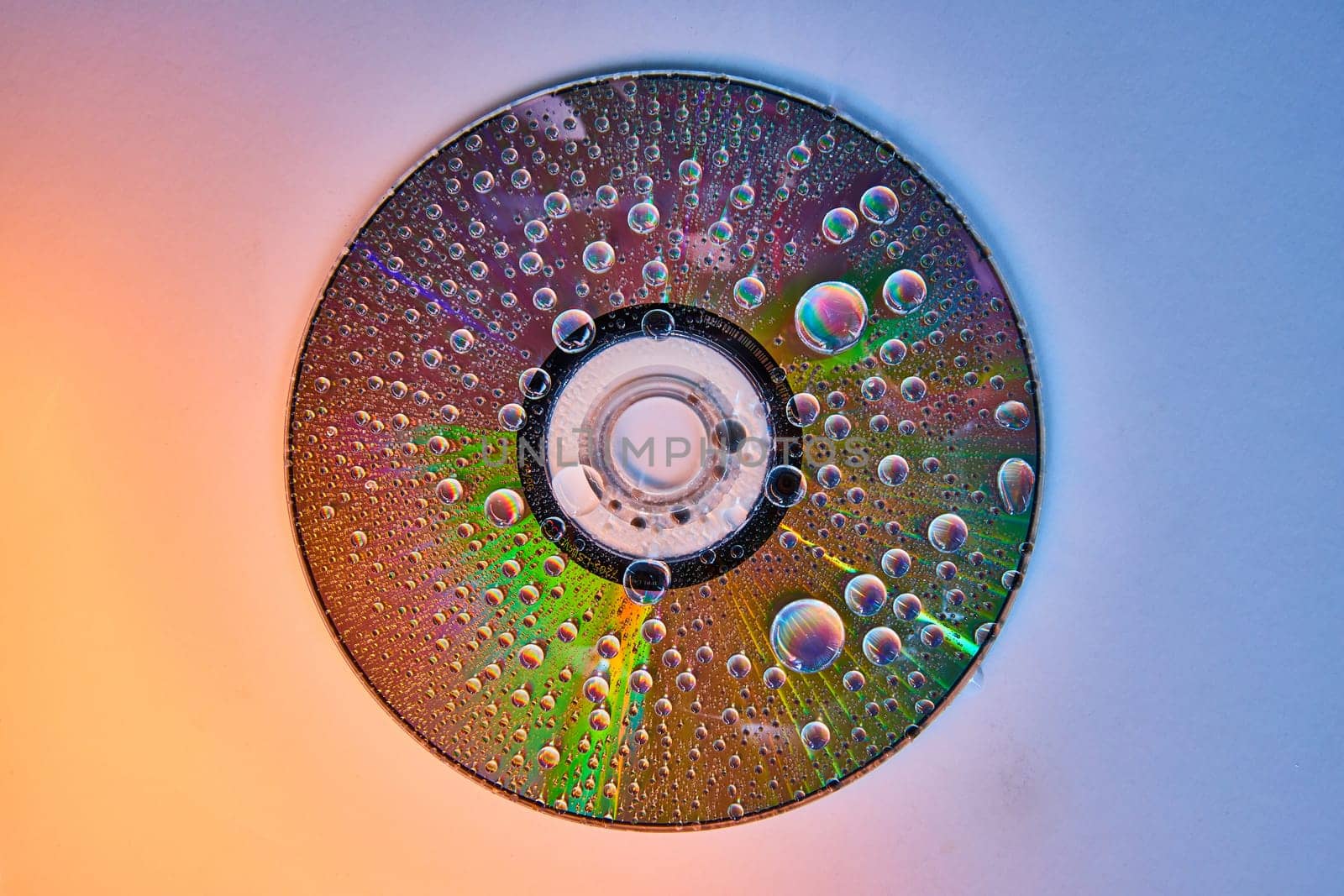 Image of CD on gradient shift background with rainbow water drops on reflective metal surface