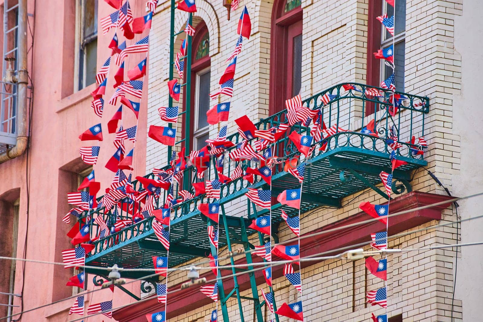 Image of Chinese and American flags in long ribbons attached to white building with green fire escape