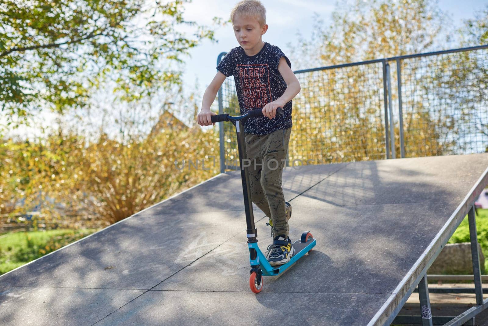 Child on kick scooter in park. Kids learn to skate roller board. Little boy skating on sunny summer day. Outdoor activity for children on safe residential street. Active sport for preschool kid. boy kid Roller park