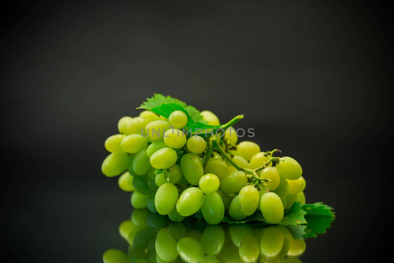 A bunch of ripe green grapes with leaves, isolated on a black background.