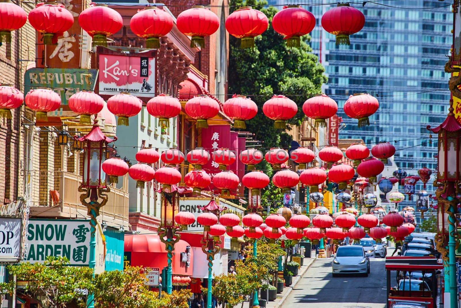 Image of Strings of red Chinese lanterns over busy road with white cars and Chinatown shops