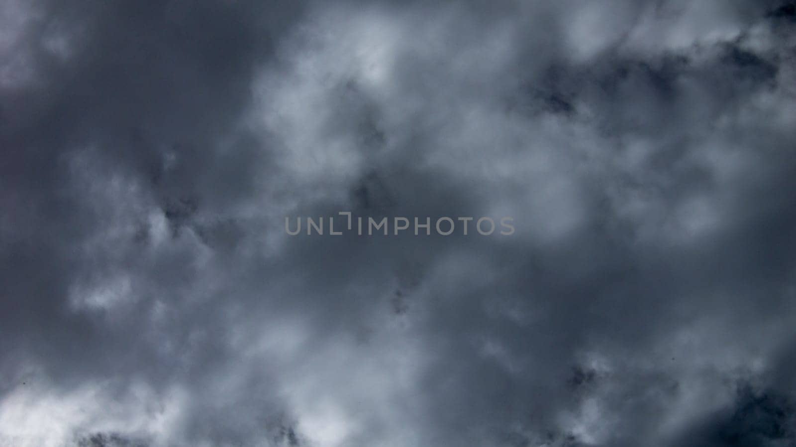 Dense, dark storm clouds loom overhead, casting shadows over a serene rural area as the afternoon light begins to fade, signaling the potential for rain.