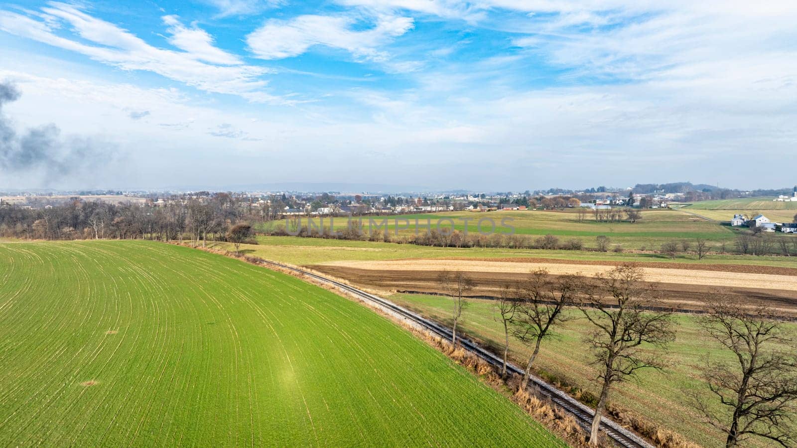 A sweeping view of lush green fields stretches out towards the horizon with scattered towns visible. The sky is partly cloudy, hinting at a peaceful day in a rural setting.