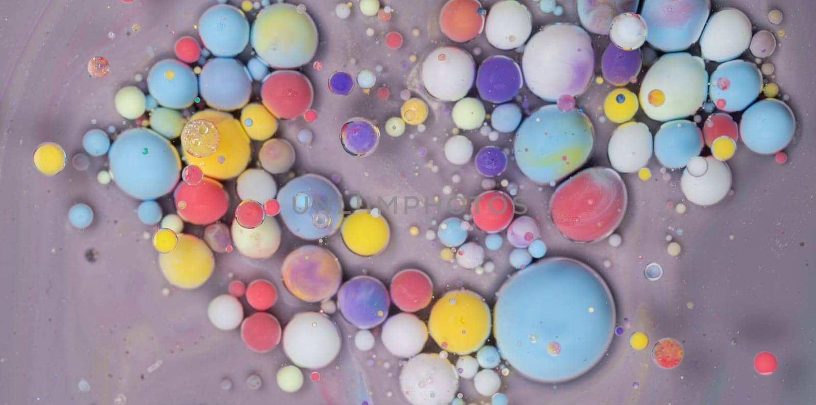 An intricate display of colorful spheres in various sizes floats on a smooth gray surface, demonstrating a captivating mix of paint and liquid. The arrangement creates an artistic abstract effect.