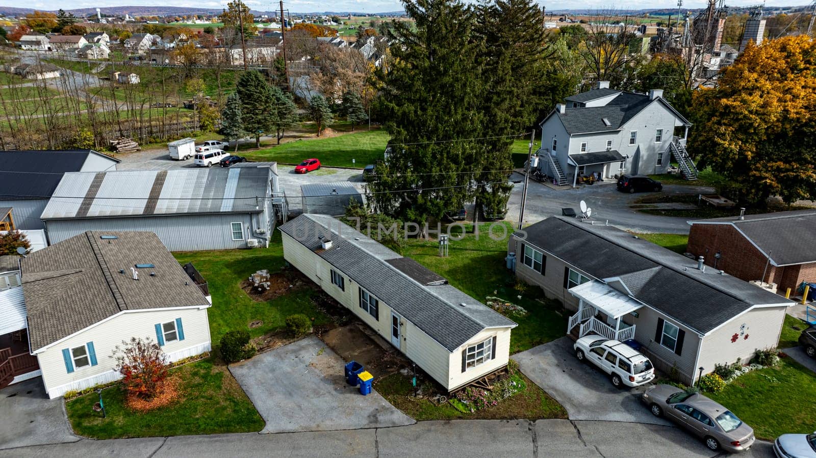 Various Mobile, Prefab, Manufactured, homes are seen in a rural setting with colorful autumn trees and a distant industrial area