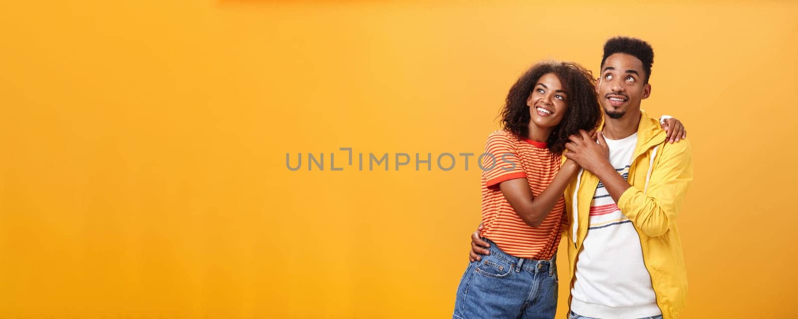 Couple of lovers enjoying spending warm summer evening together gazing up at stars with happy. enthusiastic expression being in love hugging and expressing warm romantic feelings over orange wall.