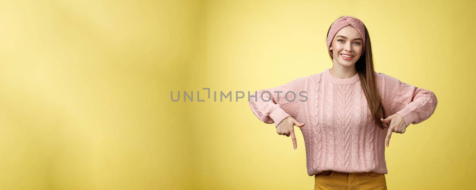Tender young 20s european girl in sweater smiling broadly finally take-off braces pointing down promoting skillful dentist professional. Female student standing happy positive over yellow wall.