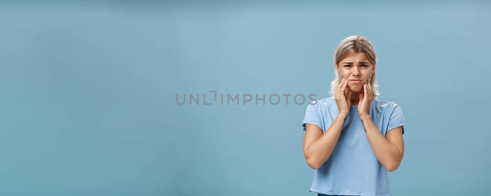 Girl feeling pain in teeth after drinking hot coffee. Displeased unhappy troubled young girl with blond hair frowning feeling discomfort in mouth holding hands on cheeks suffering toothache.