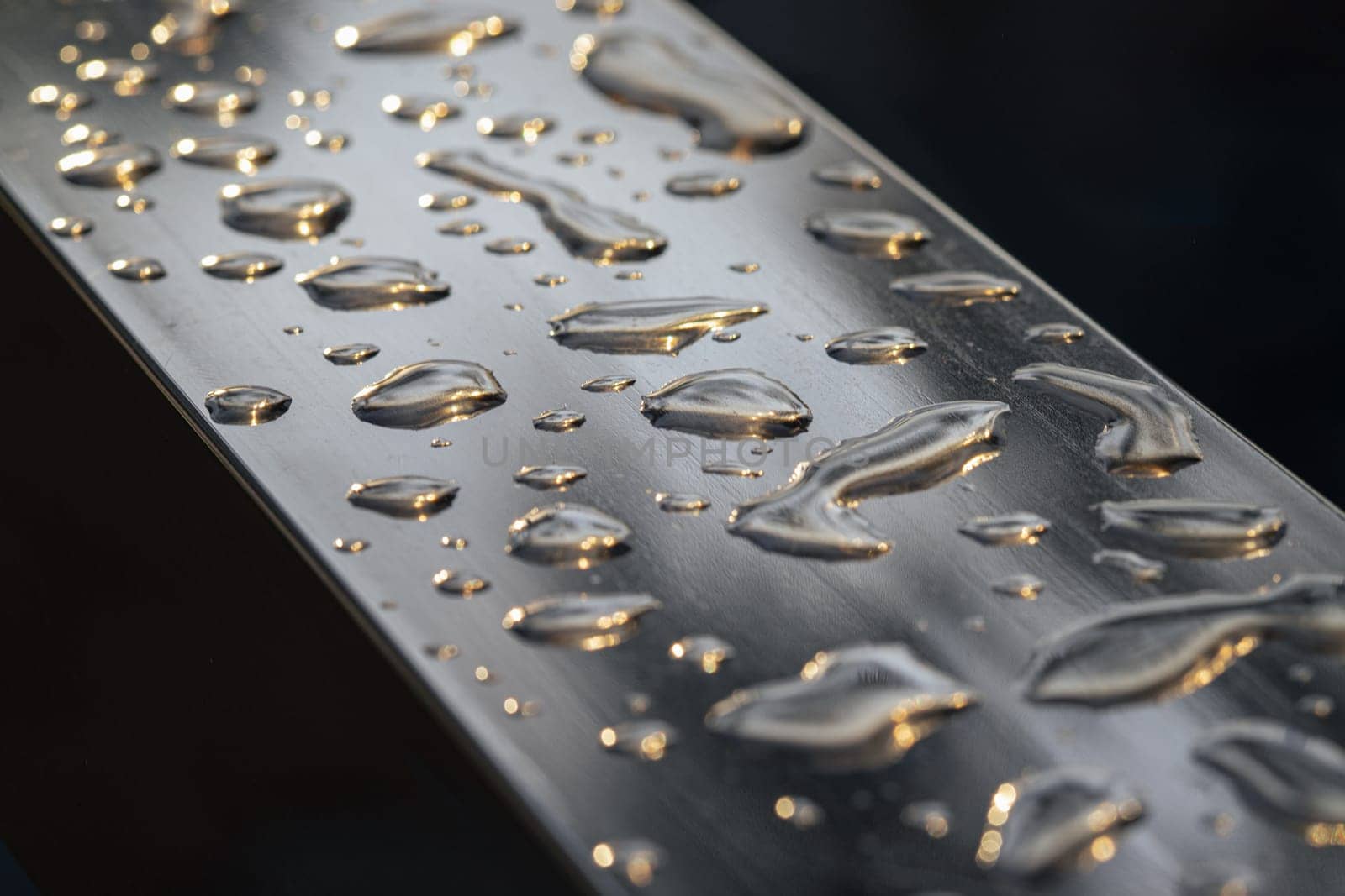 Detail of Water droplets caused by rain perched on the metallic surface. Rain water drops on a stainless steel handle, Natural Pattern of dew drops or raindrops on silver metal background for wallpaper poster and banner design, Selective focus.