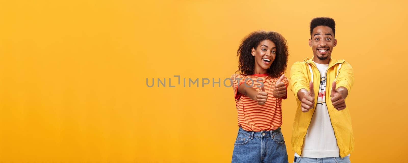 Two friends like perfect and awesome plan. Portrait of joyful friendly-looking optimistic african american female and male showing thumbs up in approval and agreement gesture smiling broadly. Copy space