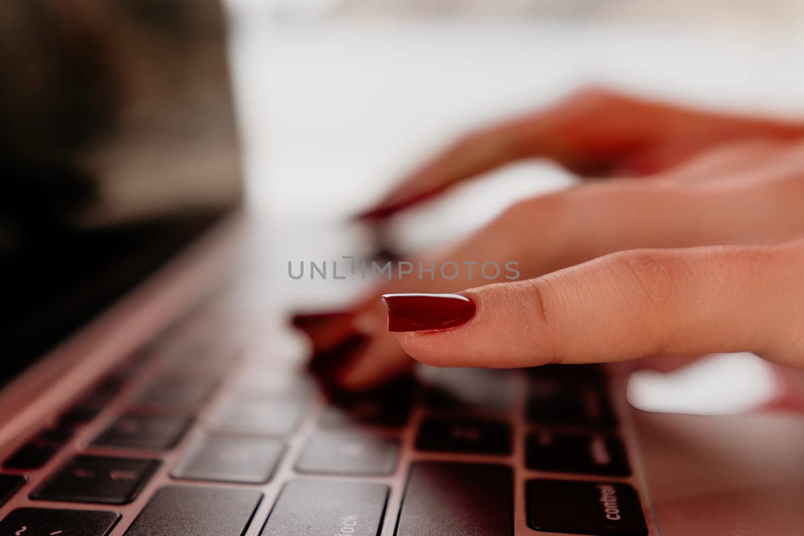 Close-up of hands with red nail polish typing on a laptop keyboard.