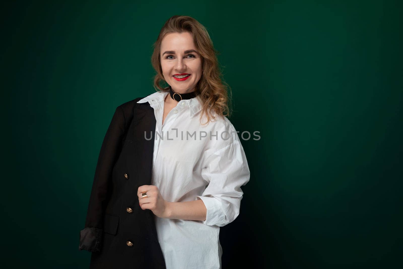 A woman standing in a white shirt and black jacket, looking directly at the camera with a neutral expression. Her outfit is professional and stylish, suitable for a formal setting.