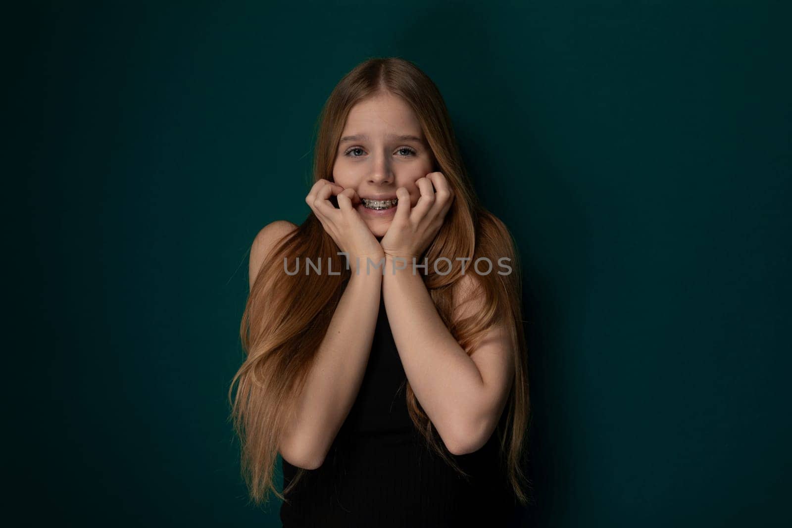 A girl with long red hair stands confidently in a pose for a photograph. She looks directly at the camera, showcasing her striking features and vibrant hair color.