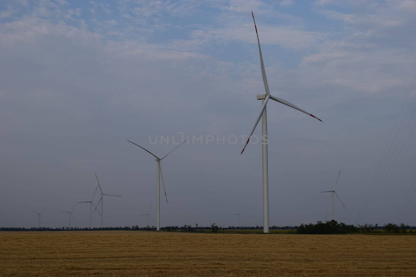 A field of windmills spin in front of a colorful evening sky. A wind turbine is used to produce electricity. Wind energy is the use of wind for electrical power. It's a sustainable, renewable energy