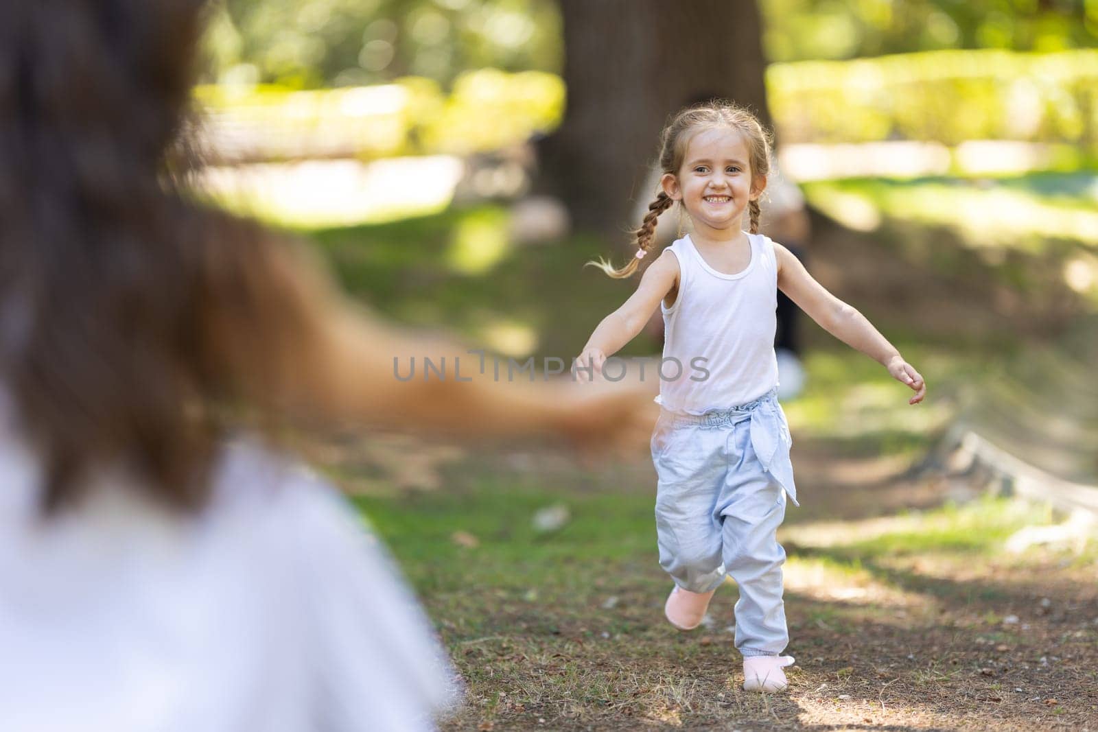 Happy little girl running through the park to her mother with open arms on a sunny summer day