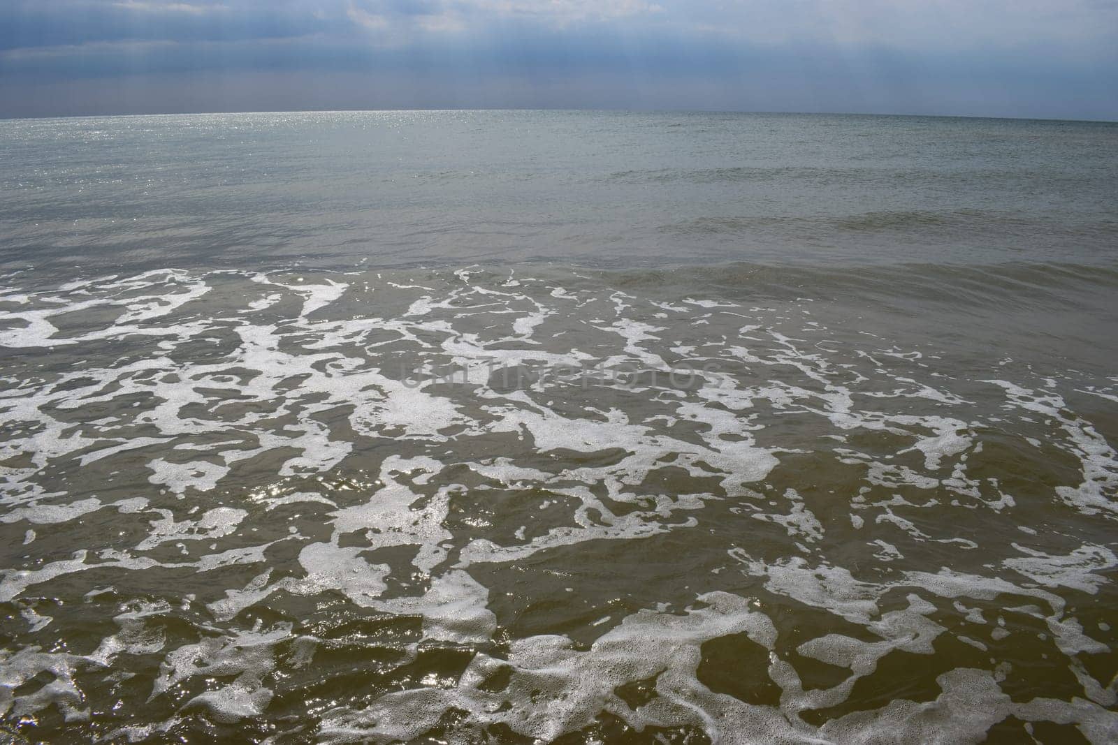 Beautiful landscape - turquoise colored sea water, sand, sky. The waves are on the sea to the shore. The Beach And Splashing Waves