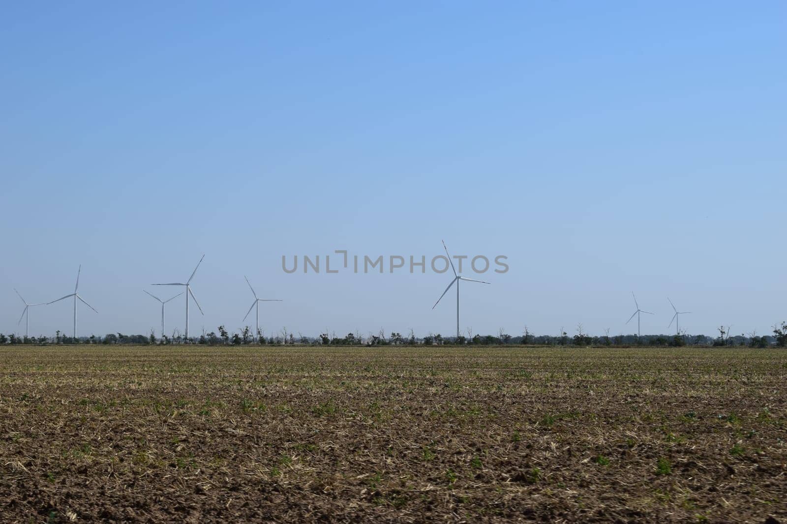 A field of windmills spin in front of a colorful evening sky. A wind turbine is used to produce electricity. Wind energy is the use of wind for electrical power. It's a sustainable, renewable energy