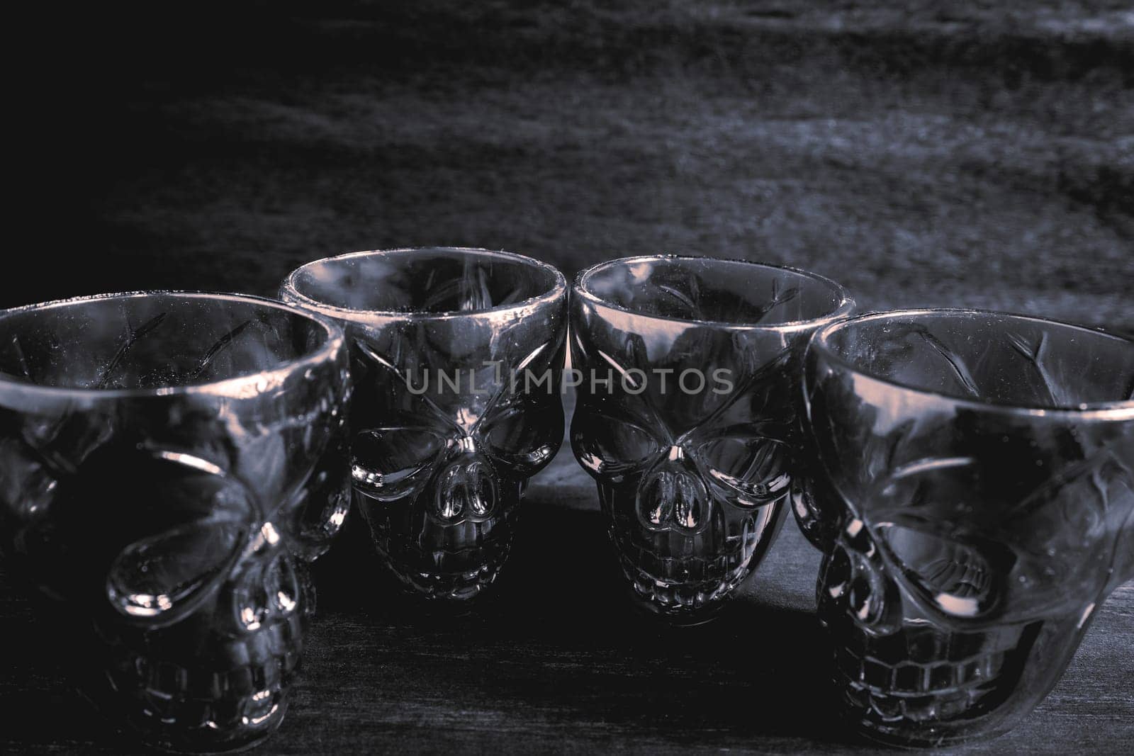 A couple of shot glasses in the shape of a skull, for a Halloween Party. On a wooden background, in black and white.