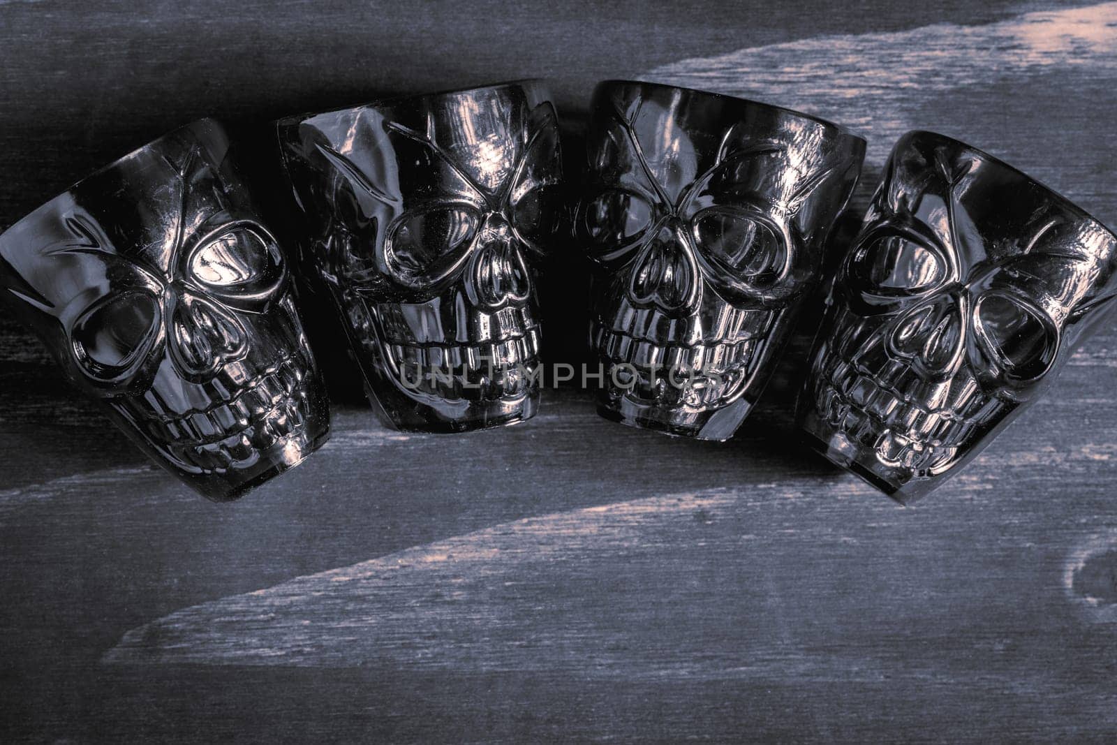 A couple of shot glasses in the shape of a skull, for a Halloween Party. On a wooden background, in black and white.