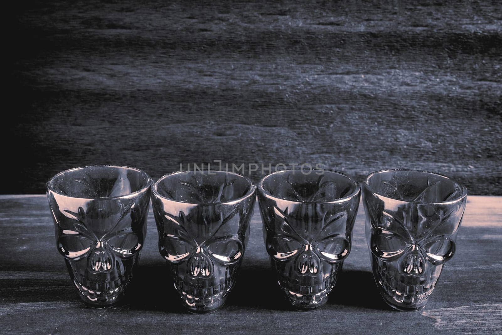 A couple of shot glasses in the shape of a skull, for a Halloween Party. On a wooden background, in black and white.