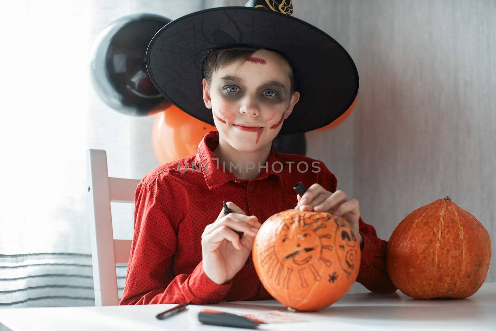 Teen boy in costume drawing coronavirus image on the pumpkin for the Halloween celebration. Halloween carnival with new reality with pandemic concept.