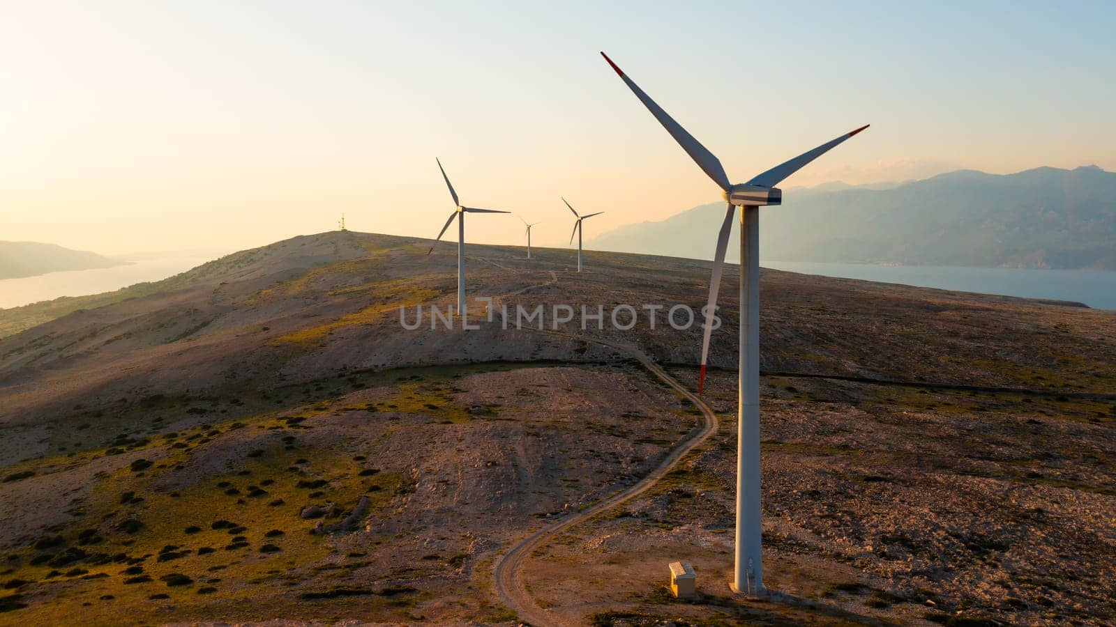 Wind turbines generate eco-friendly power on Pag Island, encircled by the Adriatic Sea at sunset.