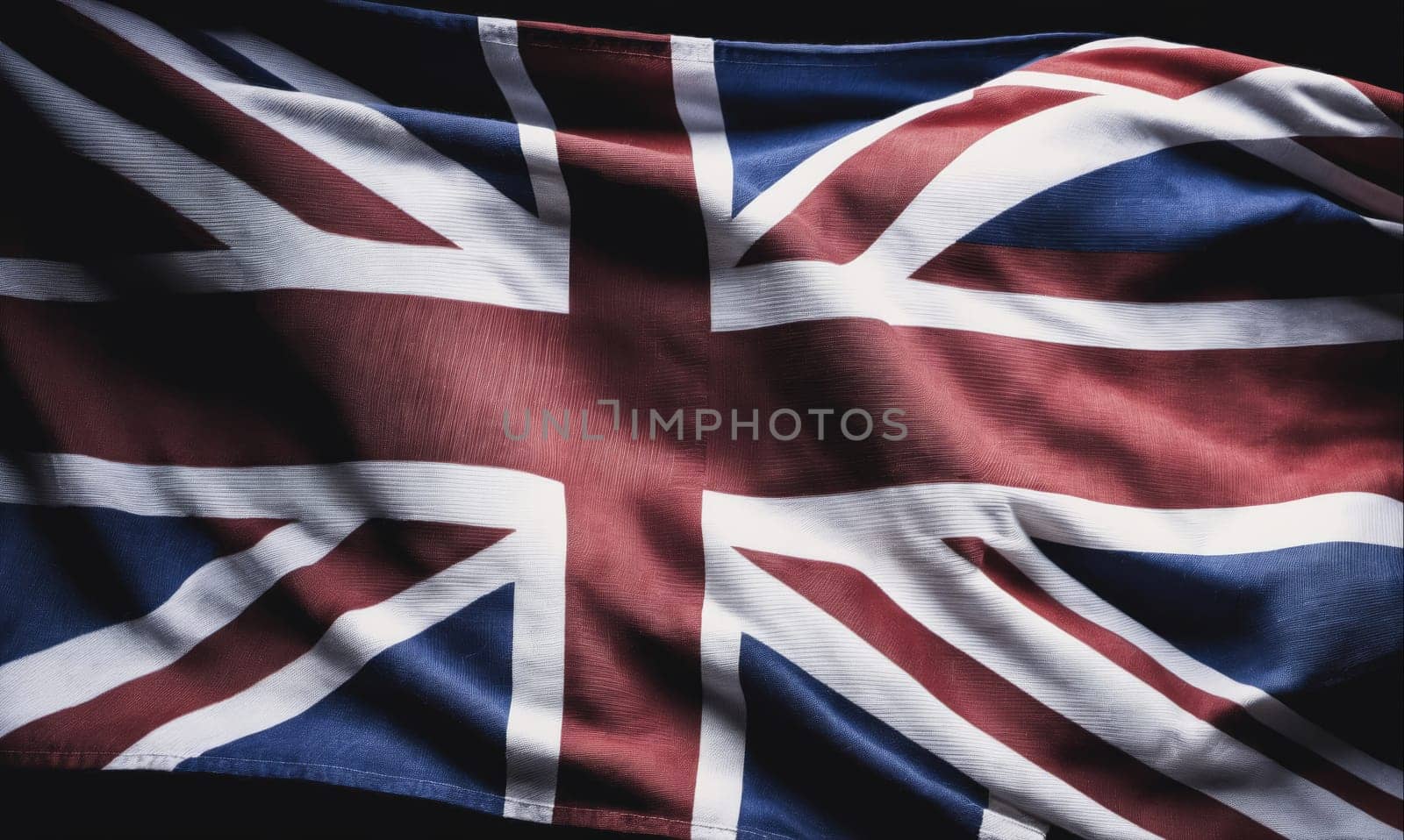 The image shows a Union Jack flag waving in the wind. The flag is made of a red, white, and blue fabric and is illuminated by a strong light source, creating a dramatic contrast against the dark background.