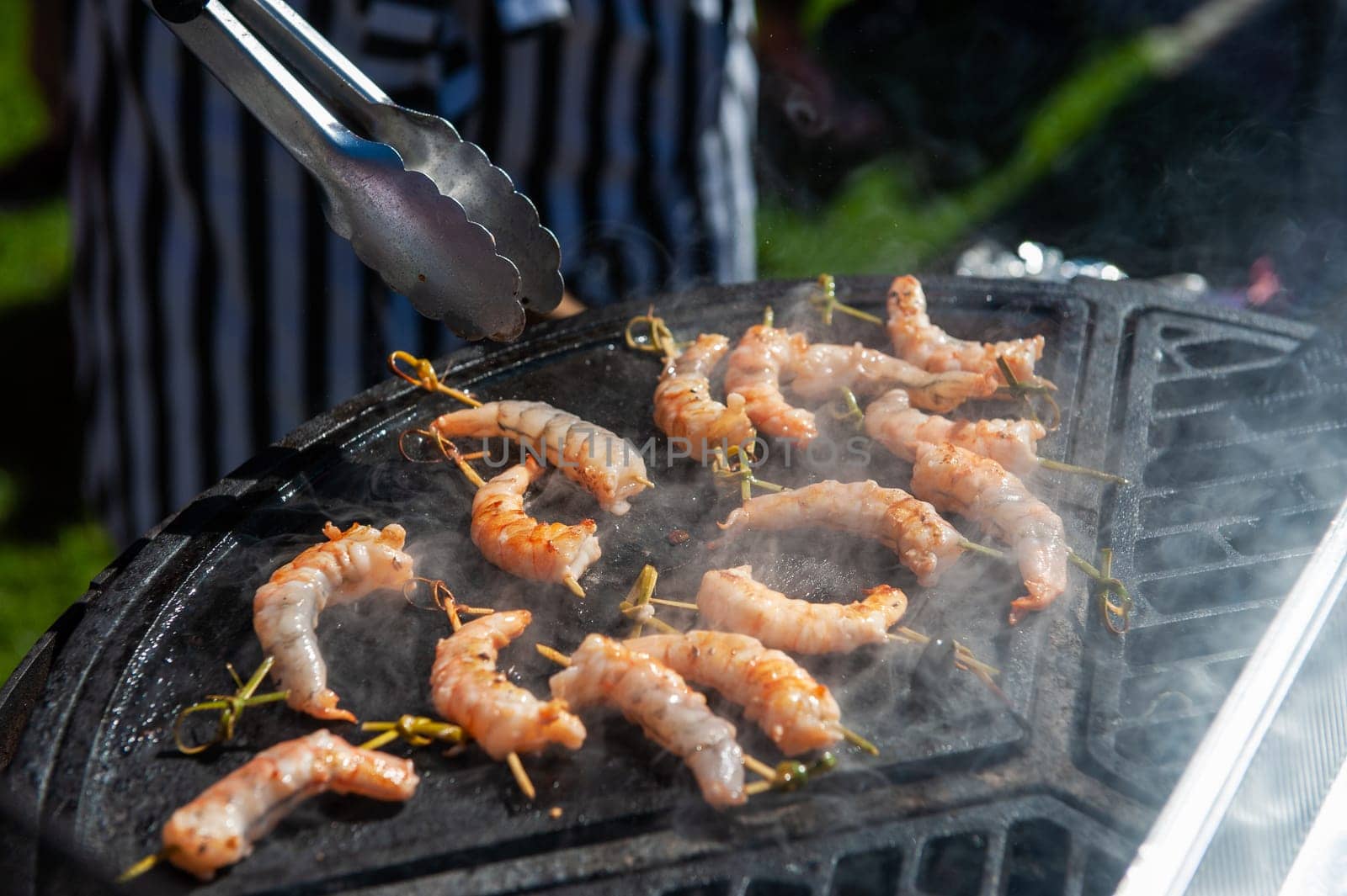 A professional cook prepares shrimps on the grill outdoor, food or catering concept