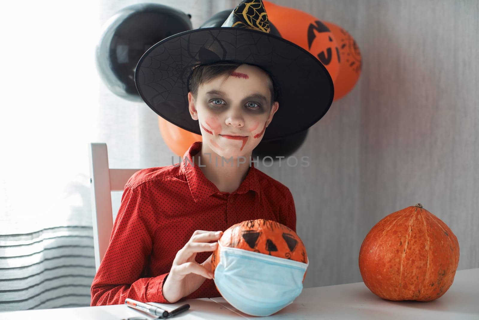 Teen boy in costume and face masks to protect against COVID-19 drawing a pumpkin for the Halloween celebration. Halloween carnival with new reality with pandemic concept.