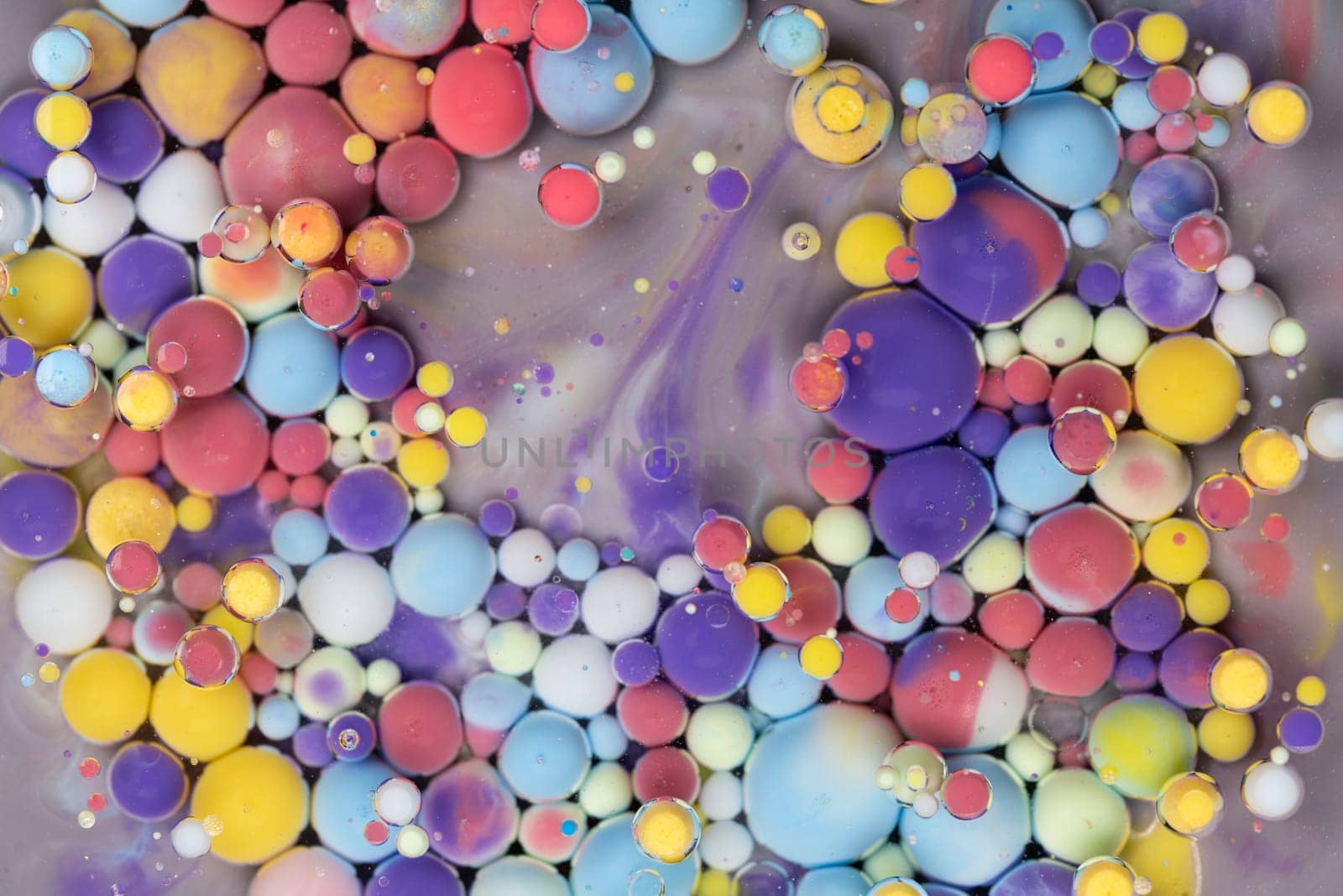 Bright and colorful droplets of paint float on a surface, forming abstract patterns. The composition features an array of sizes and colors, showcasing artistic creativity.