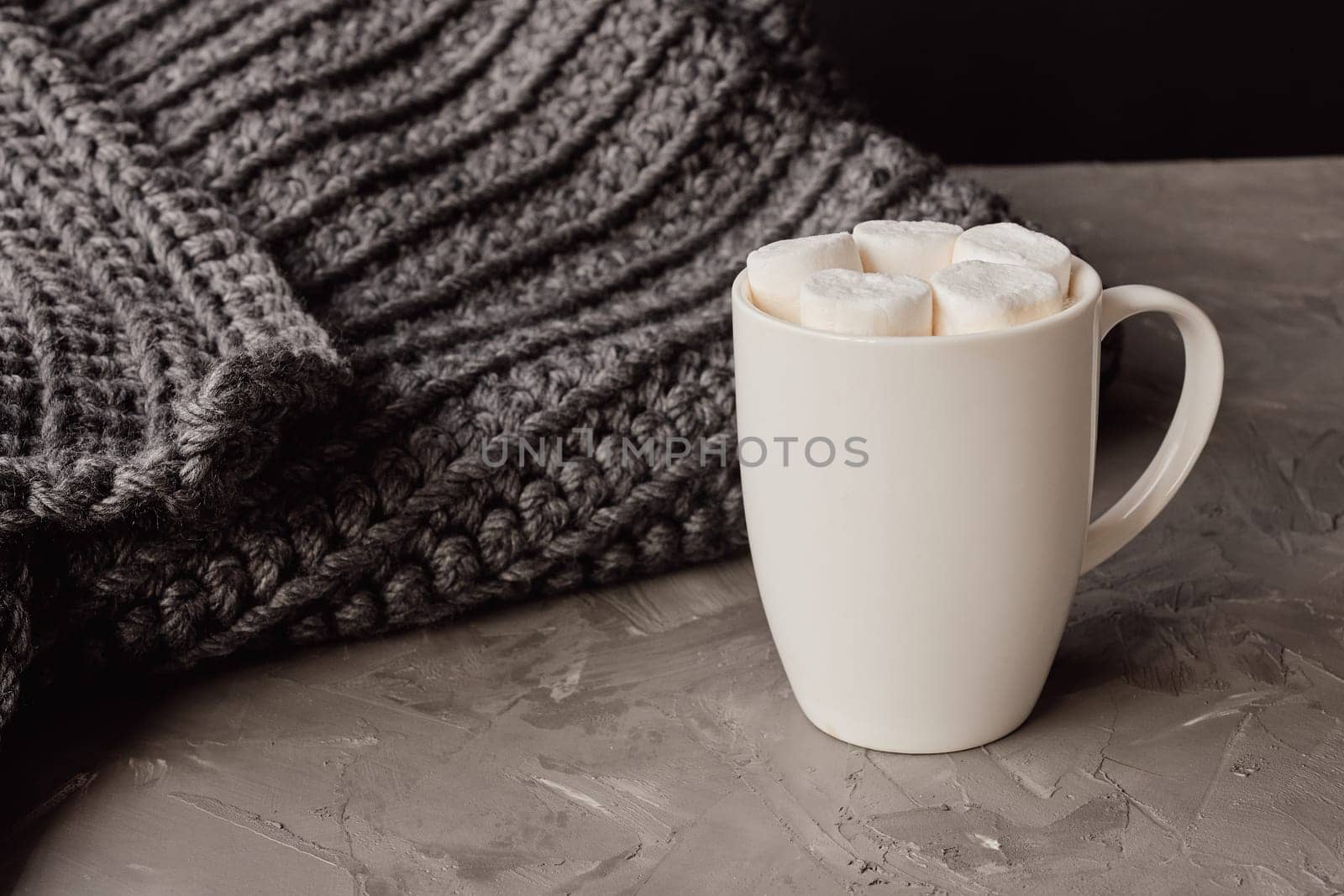 Creating a warm atmosphere with a cup of hot cocoa, marshmallows, and a cozy grey knitted blanket for relaxation