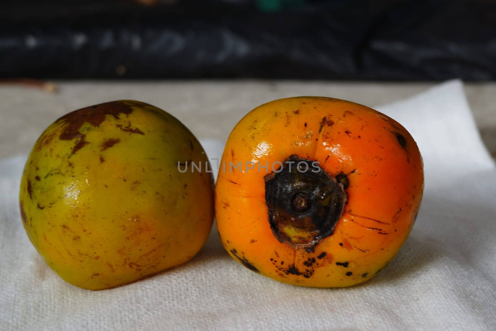 The image shows two round, orange persimmon fruits stacked on a white paper towel.
